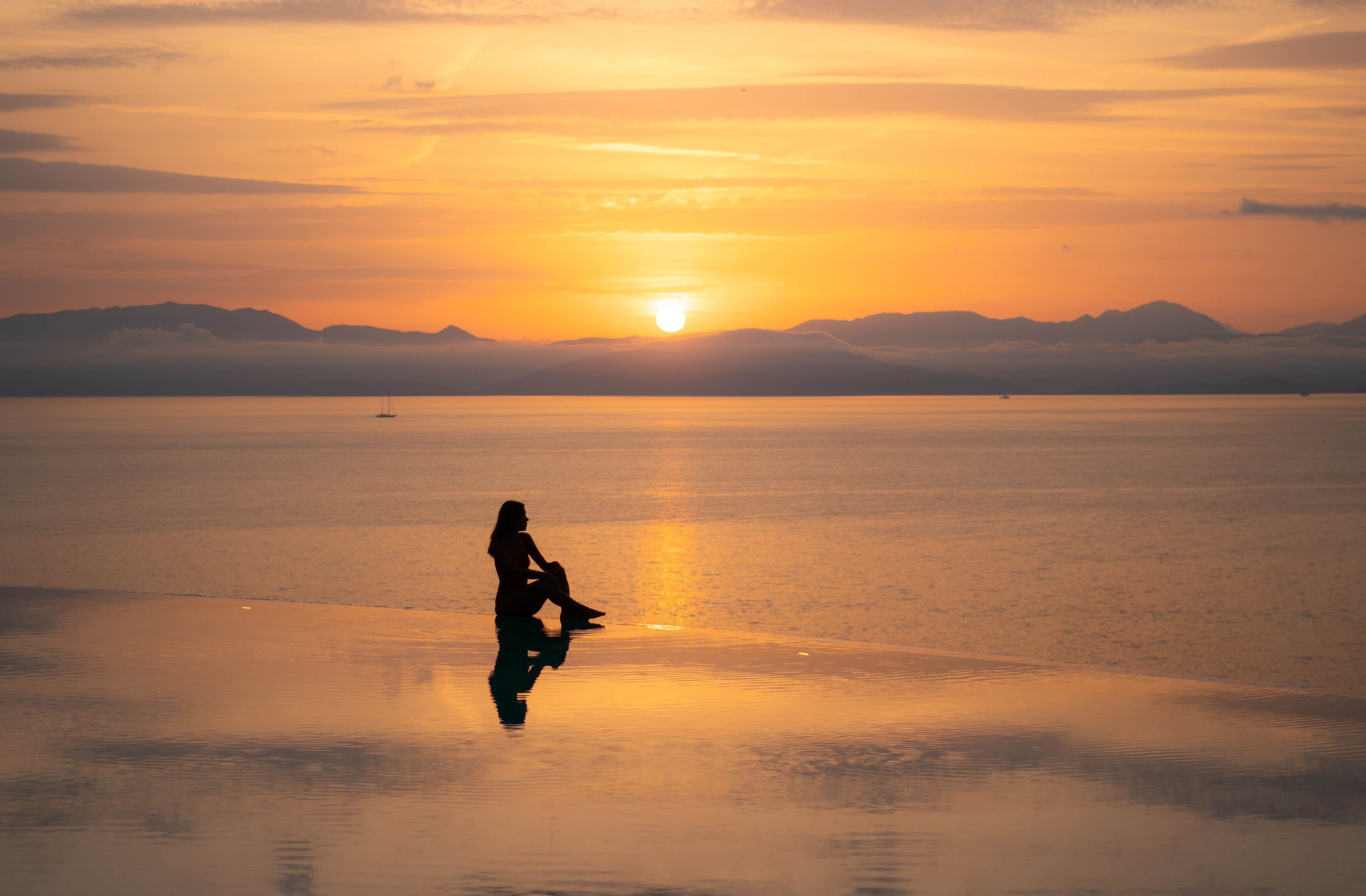 girl sitting at the infinity pool of angsana corfu during sunrise 
